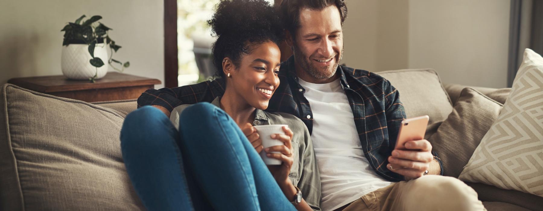 a man and woman sitting on a couch and looking at a cell phone