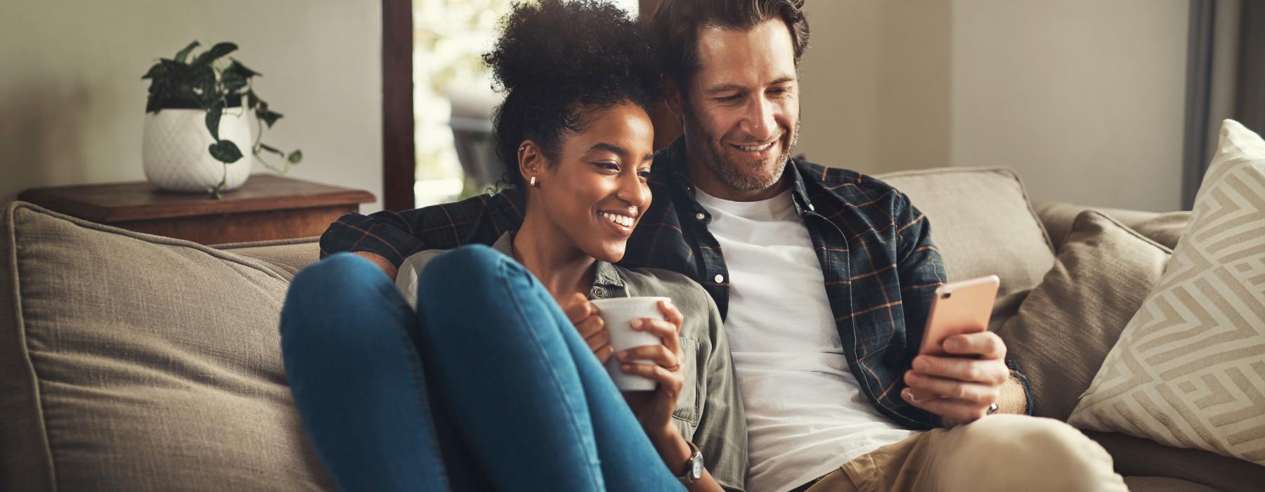 a man and woman sitting on a couch and looking at a cell phone